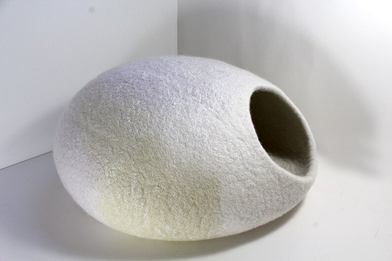 May include: A white felt cat bed shaped like an egg with a large opening on one side. The bed is made of a soft, fluffy material and is perfect for cats to curl up in.