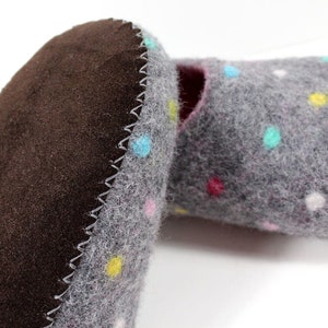 May include: A pair of gray felt slippers with colorful polka dots. The slippers have a brown suede sole and a zig-zag stitch around the edge.