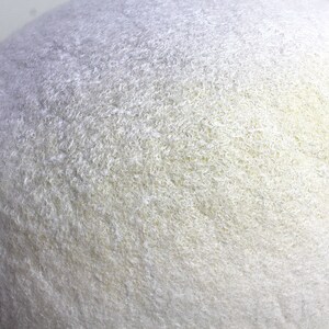 May include: A white felt cat bed shaped like a cave. The bed has a soft, fuzzy texture and a light yellow hue.
