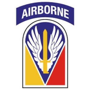 May include: A blue and white patch with the word "AIRBORNE" in white letters. The patch features a white sword with wings on a blue background with a yellow and red triangle.