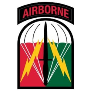 Puede incluir: Un parche rojo, blanco y verde con un paracaídas, rayos y una daga. El texto "AIRBORNE" está por encima del parche.