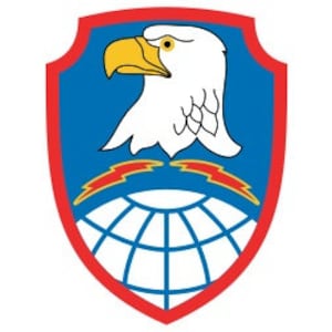May include: A blue and white eagle with a yellow beak and red eyes is centered on a blue shield with a red border. The eagle is above a globe with two lightning bolts. The globe is surrounded by a red border.