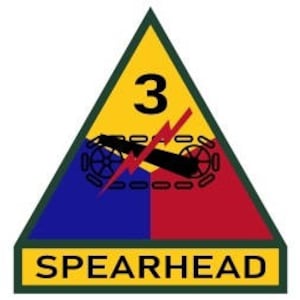 May include: A yellow triangle with the number 3 inside, a blue and red background, and a black cannon with a lightning bolt over it. The text "SPEARHEAD" is below the triangle.