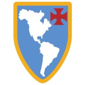 Puede incluir: Un escudo azul y amarillo con un contorno blanco, que representa un contorno blanco de las Américas. Una cruz roja se encuentra en la esquina superior derecha del escudo.