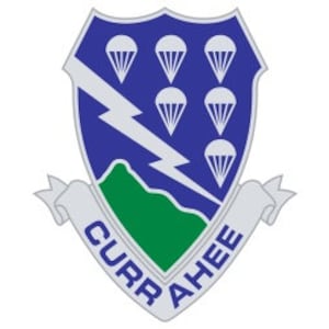 Pode incluir: Um remendo de unidade militar azul e verde com um raio, montanhas e seis paraquedas. O texto "CURAHEE" está em uma faixa branca.