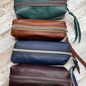 May include: Four leather zippered pouches in different colors: teal, brown, navy blue, and burgundy. Each pouch has a zipper closure and a small leather strap.