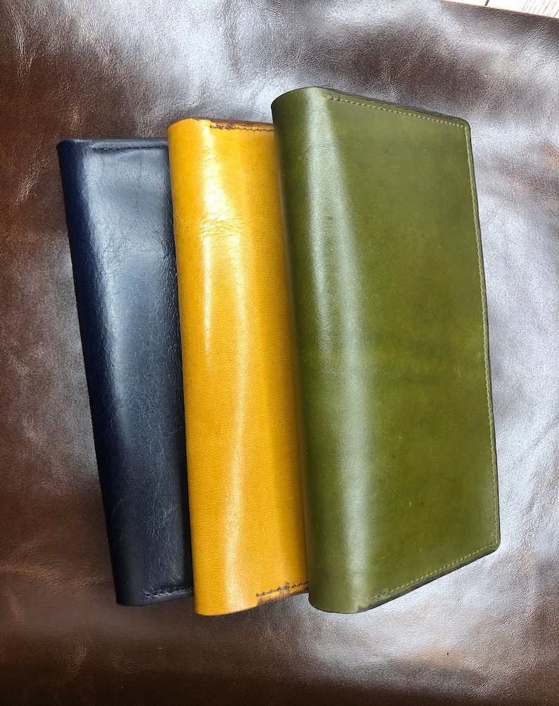 May include: Three leather wallets in different colors: navy blue, yellow, and green. The wallets are stacked on top of each other.
