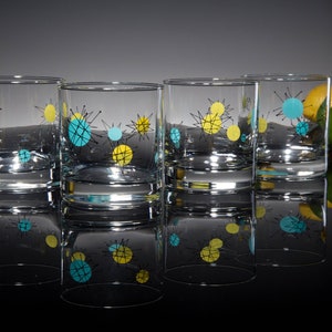 May include: Four clear glass tumblers with a mid-century modern design. The glasses feature a black, yellow, and turquoise geometric pattern.