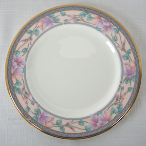 Puede incluir: Un plato de cerámica blanco con un borde dorado y un diseño floral rosa y azul. El plato tiene un delicado patrón floral con flores rosas y azules y hojas verdes.