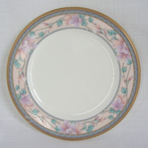 Puede incluir: Un plato de cerámica blanco con un diseño floral rosa y morado. El plato tiene un borde dorado y un borde azul y dorado.