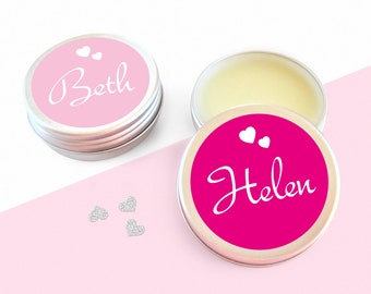 Könnte beinhalten: Zwei kleine silberne Dosen mit rosa und roten Deckeln. Die Deckel haben weiße Herzen und die Namen "Beth" und "Helen" in weißer Schrift.