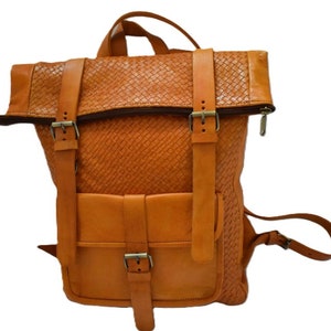 May include: A brown leather backpack with a woven design and multiple buckles. The backpack has a flap that folds over the top and a zipper closure.