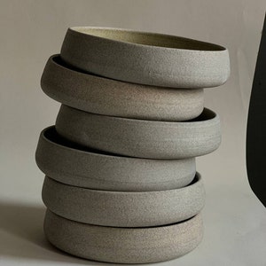 May include: A stack of six ceramic bowls in various shades of gray, with a slightly textured surface. The bowls are stacked in a graduated size, with the largest bowl at the bottom and the smallest bowl at the top.