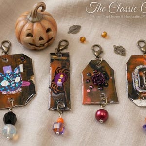 May include: A collection of artisan bag charms with a Halloween theme. The charms feature mixed media designs with a cat, a candle, and a rose. A small pumpkin and decorative leaves are also present.