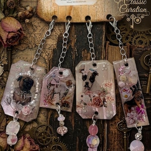 May include: Four rectangular and pentagonal bag charms featuring vintage-style dog illustrations, floral accents, and pearl embellishments. Each charm hangs from a silver-tone chain with a lobster clasp and a dangling bead charm at the bottom.
