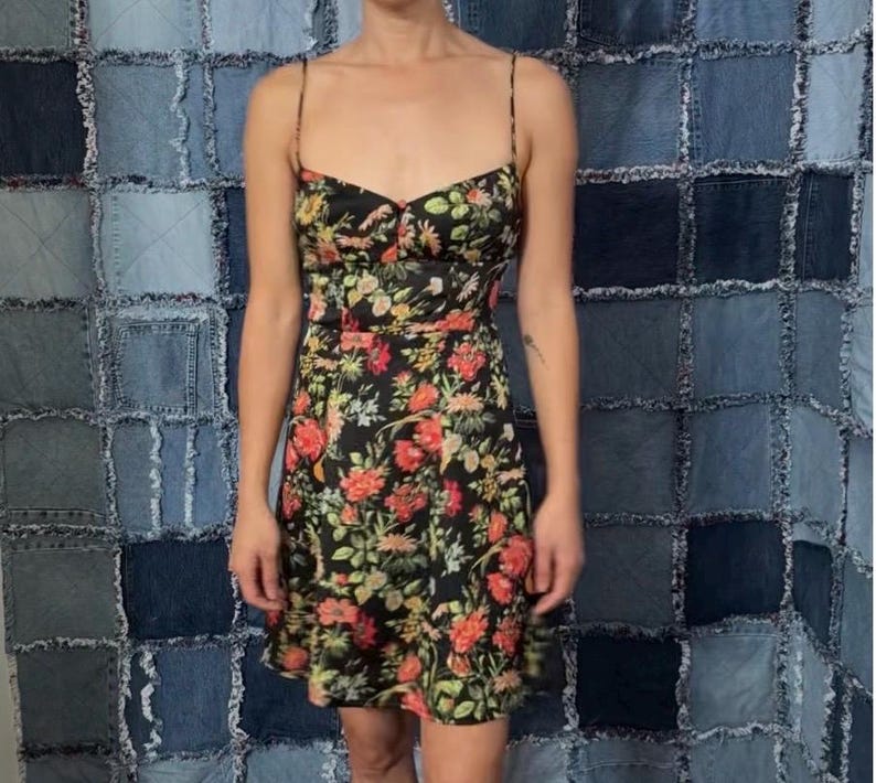 May include: A black floral print dress with spaghetti straps. The dress features a fitted bodice and a flared skirt, with a pattern of red, orange, and green flowers. The dress is made of a lightweight fabric.