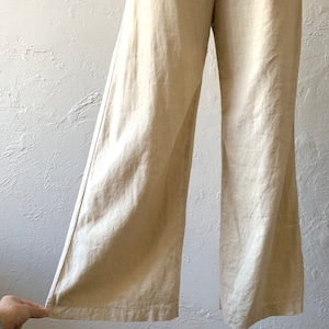 May include: Wide-leg pants in a light beige linen fabric. The pants have a high waist and a tie belt.