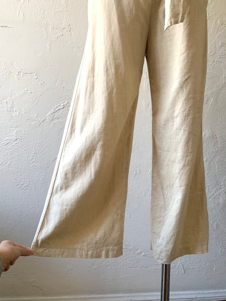May include: Wide-leg pants in a light beige linen fabric. The pants have a high waist and a tie belt.