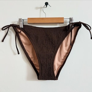 May include: Brown bikini bottom with adjustable ties. The bottom is made of a textured fabric.