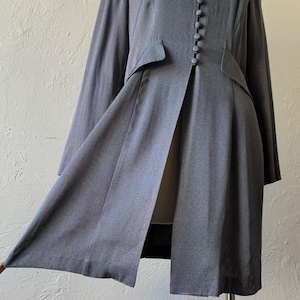May include: A long, gray, button-front coat with a center slit and a fitted waist.