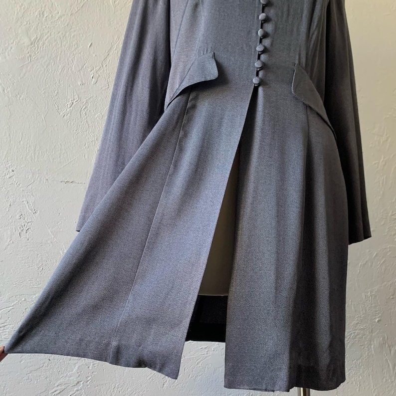 May include: A long, gray, button-front coat with a center slit and a fitted waist.