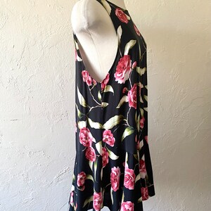 May include: A sleeveless black dress with a floral print of pink roses and green leaves. The dress has a ruffled hem.