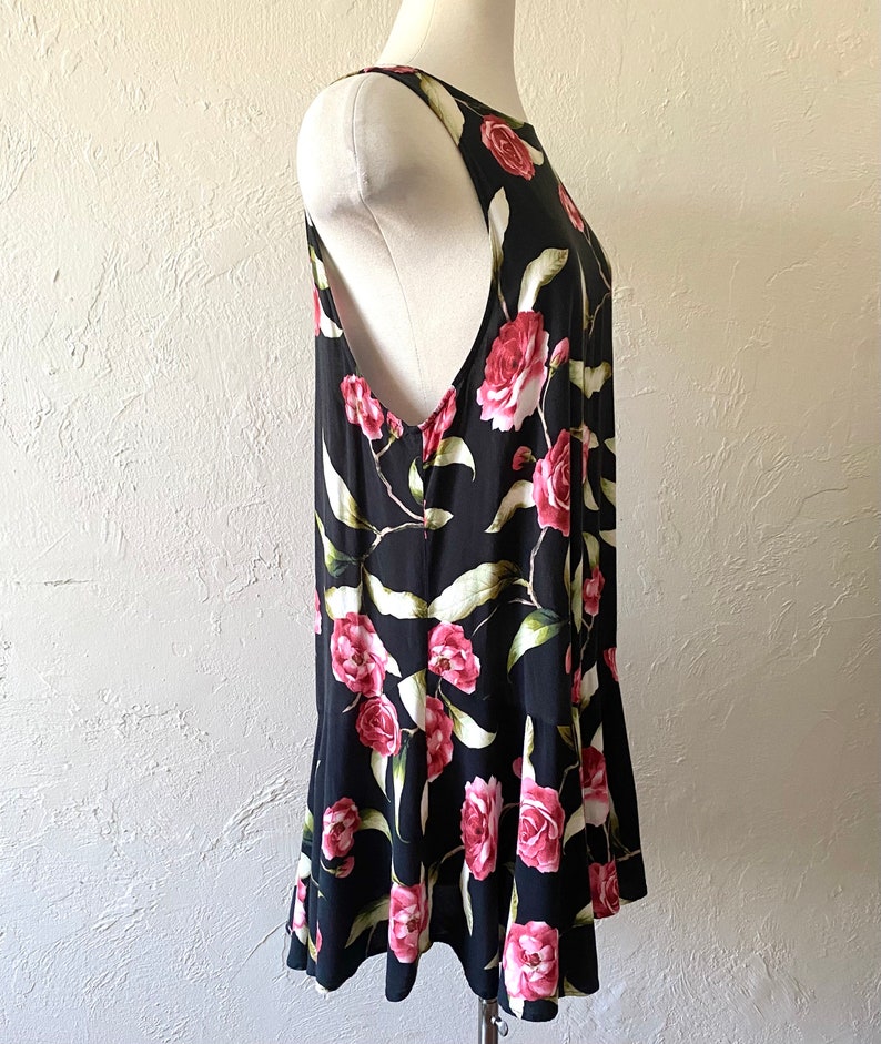 May include: A sleeveless black dress with a floral print of pink roses and green leaves. The dress has a ruffled hem.