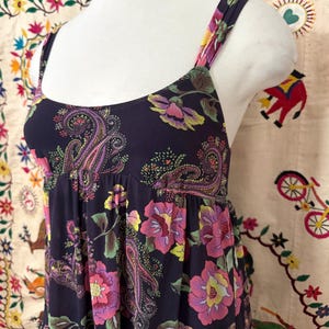 May include: A sleeveless maxi dress with a dark purple background and a floral print. The dress has a paisley pattern and features pink, yellow, and green flowers.
