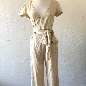 May include: A beige linen wrap top and wide-leg pants set with a tie at the waist.
