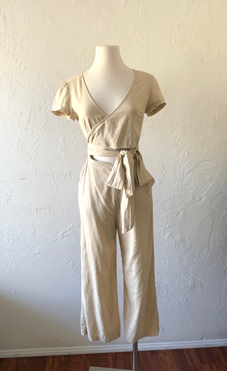 May include: A beige linen wrap top and wide-leg pants set with a tie at the waist.