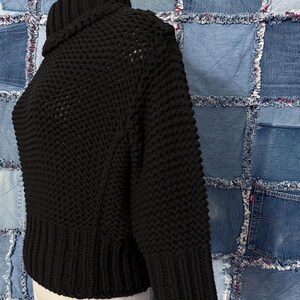 Puede incluir: Un su&eacute;ter negro de punto grueso con cuello alto. El su&eacute;ter tiene un dobladillo y pu&ntilde;os acanalados, y un patr&oacute;n de puntada texturizada en el cuerpo y las mangas. La prenda se exhibe en un maniqu&iacute;.
