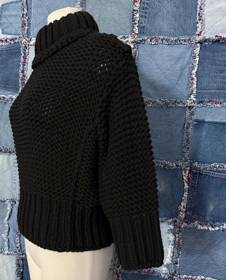 Puede incluir: Un su&eacute;ter negro de punto grueso con cuello alto. El su&eacute;ter tiene un dobladillo y pu&ntilde;os acanalados, y un patr&oacute;n de puntada texturizada en el cuerpo y las mangas. La prenda se exhibe en un maniqu&iacute;.