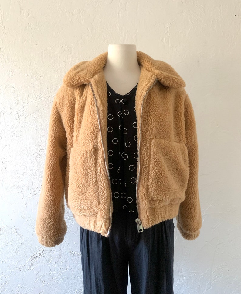 K&ouml;nnte beinhalten: Eine braune Kunstfelljacke mit Rei&szlig;verschluss und zwei Taschen. Die Jacke hat eine verk&uuml;rzte Passform und einen Kragen.
