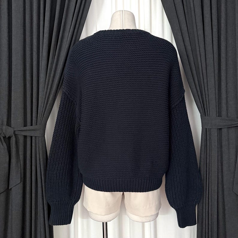 May include: A navy blue knit sweater with a crew neck and long sleeves. The sweater has a textured knit pattern and is displayed on a mannequin. The sleeves are slightly puffed at the shoulders.