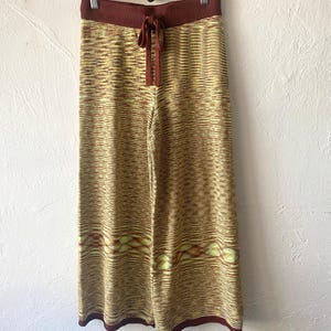 May include: Wide-leg knit pants with a brown waistband and a tie at the waist. The pants have a yellow and brown striped pattern with a geometric design at the bottom.