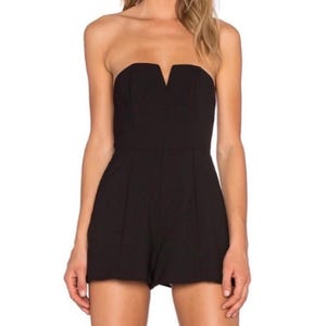 Może przedstawiać: Czarny kombinezon bez ramiączek z dekoltem w kształcie litery V. Kombinezon ma dopasowany gorset i szorty. Ubranie wykonane jest z jednolitego, ciemnego materiału.