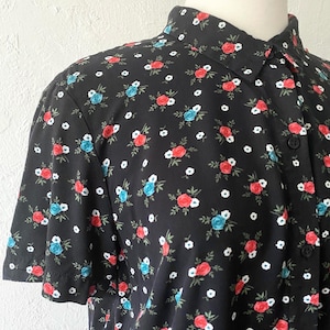 May include: A black short-sleeved button-up shirt with a floral print featuring red, blue, and white flowers.