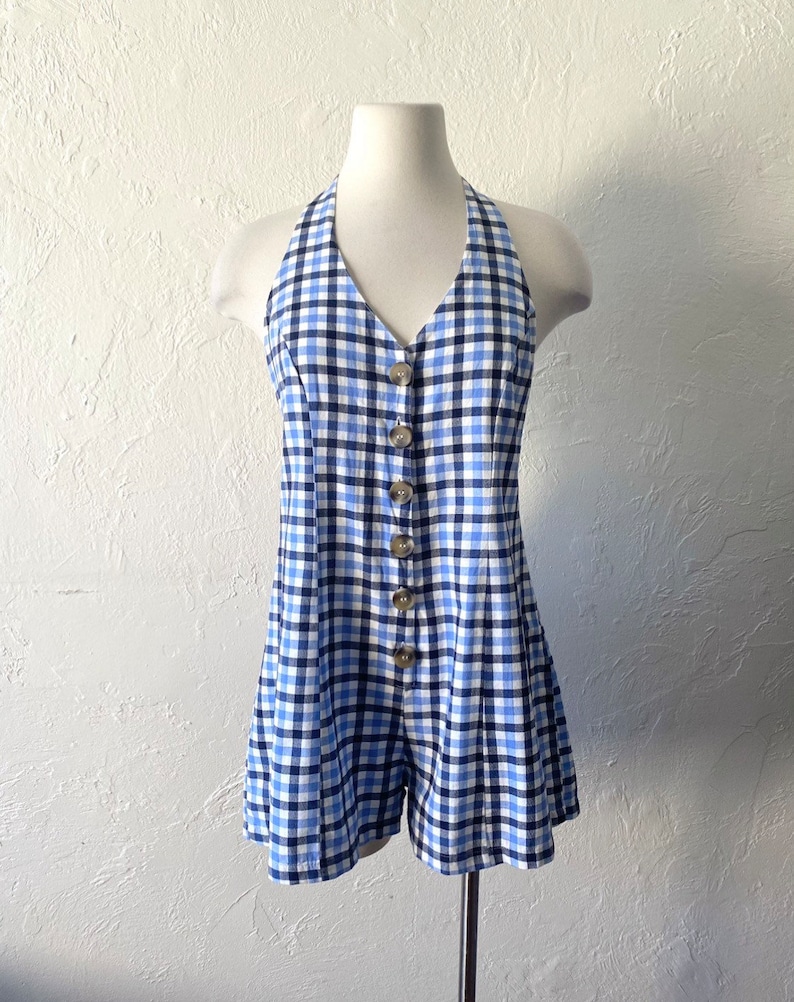 Puede incluir: Un mono azul y blanco de cuadros vichy con un estilo halter y cierre de botones en la parte delantera.