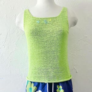 K&ouml;nnte beinhalten: Ein limettengr&uuml;nes Tanktop mit quadratischem Ausschnitt. Das Oberteil ist mit kleinen gestickten Blumen in Blau- und Gelbt&ouml;nen verziert. Der untere Teil des Oberteils ist ein blaues Blumenmuster.