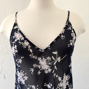 May include: A black sheer sleeveless top with a floral print. The flowers are white and pink with green stems.