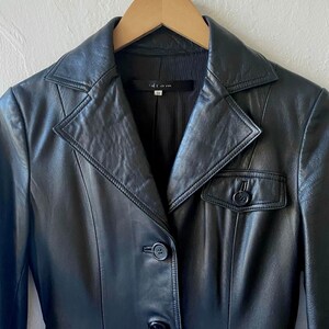 May include: A black leather blazer with a notched collar, button closure, and a small pocket. The blazer is hanging on a wooden hanger. The label inside the blazer reads "idrom".