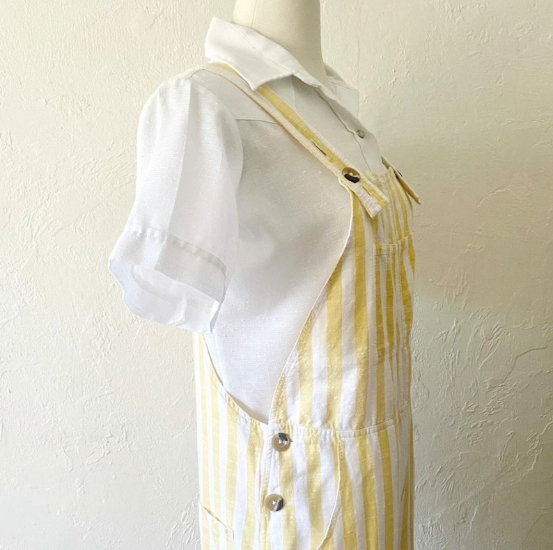 May include: White and yellow striped overalls with a white collared shirt. The overalls have adjustable straps and multiple pockets.