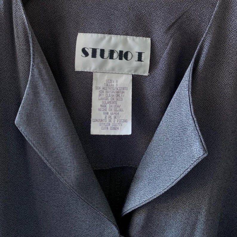 May include: A gray Studio I blouse with a collar and a tag that reads "Size: 8 Talla: 8 55% Acetate/Acetato 45% Rayon/Raton Dry Clean Only/Lando en Seco Solamente Made in USA/Hecho en EE.UU. F 66464 2 PC Set/Conjunto de 2 Piezas Style# 331776 CUTA 22824"