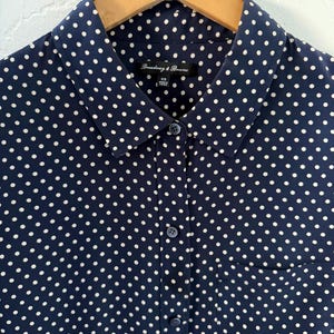 Op de afbeelding: Een donkerblauw gebloemd overhemd met een witte zak. Het overhemd heeft een kraag en een label met de tekst "Broadway & Broome" met de maat "XS" erop gedrukt.