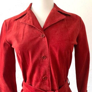 May include: A red suede shirt with a long sleeve and a button-up front. The shirt has a collar and a belt.