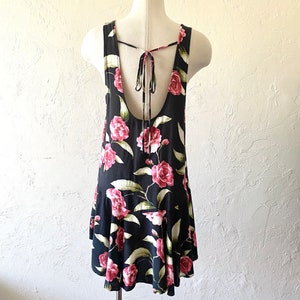 May include: A black sleeveless dress with a floral print featuring pink roses and green leaves. The dress has a tie back and a ruffled hem.