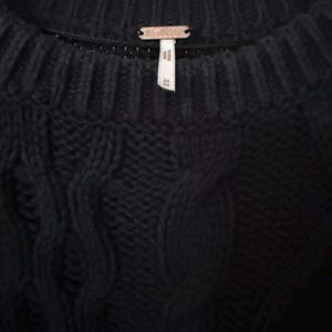 May include: Close-up of a black knit sweater with a cable knit design. The sweater has a ribbed neckline and a small metal tag with the brand name. The tag is centered at the back of the neck. The sweater is a size small.