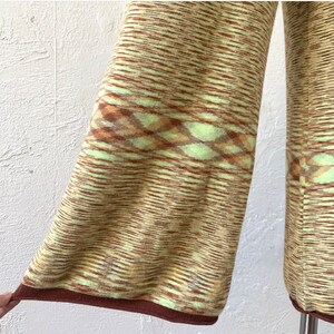 May include: A pair of wide-leg pants with a brown and green striped pattern. The pants have a brown trim at the bottom and a geometric pattern in the middle.