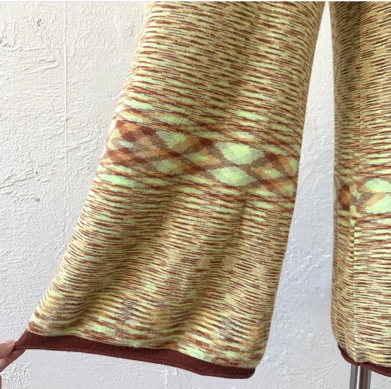 May include: A pair of wide-leg pants with a brown and green striped pattern. The pants have a brown trim at the bottom and a geometric pattern in the middle.