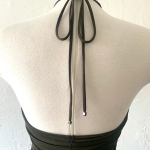 Puede incluir: Un top verde oscuro de tirantes con cierre de nudo en la espalda. El top est&aacute; hecho de una tela el&aacute;stica y tiene una silueta ajustada.